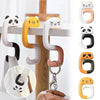 A set of portable bag hooks in various colors including black, white, yellow, and beige, shown hanging on a wooden surface.