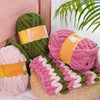 A collection of chunky chenille yarn in pink, green, and orange colors displayed on a woven mat.