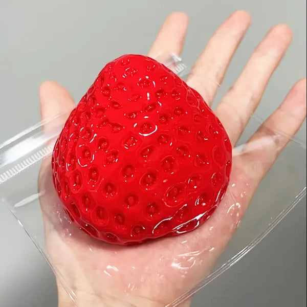 A bright red, textured strawberry squishy toy is held in a person's hand, packaged in clear plastic.