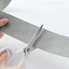 A hand uses scissors to apply a self-adhesive fiberglass screen repair patch onto a mesh material.