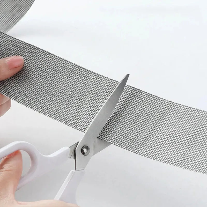 A hand uses scissors to apply a self-adhesive fiberglass screen repair patch onto a mesh material.
