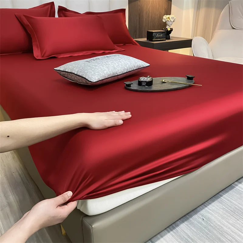 Primer plano de un juego de sábanas ajustadas de algodón rojo de lujo sobre una cama con almohadas y accesorios.