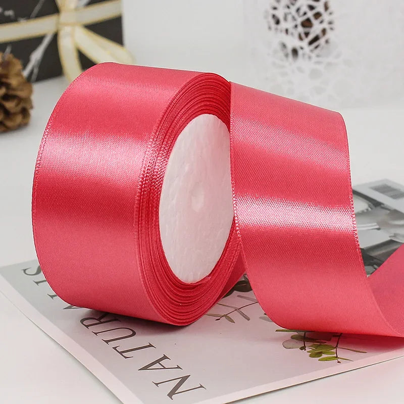 A roll of vibrant pink satin ribbon used for gift wrapping or DIY crafts, shown on a white surface.