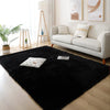 A black faux fur accent rug placed on a light wood floor in a modern living room setting.