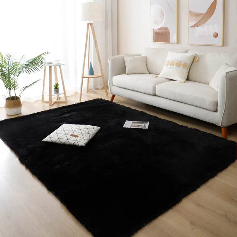 A black faux fur accent rug placed on a light wood floor in a modern living room setting.