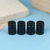 A set of four black bullet shell tire valve stem caps resting on a light blue surface next to a wooden block.