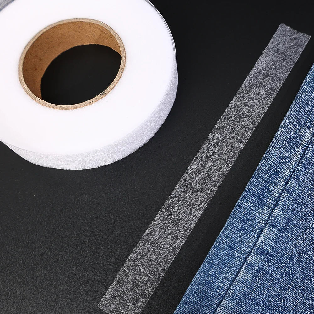 Roll of clear double-sided iron-on fabric adhesive tape next to a piece of denim fabric