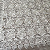 White lace tablecloth featuring an embroidered rose pattern on a wooden surface.