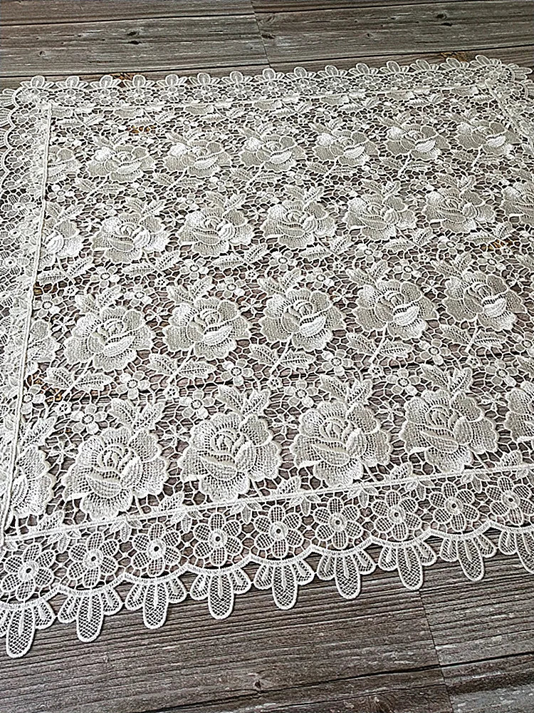 White lace tablecloth featuring an embroidered rose pattern on a wooden surface.
