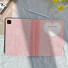 A pink composition notebook iPad case with a pencil holder is shown on a light gray fabric.