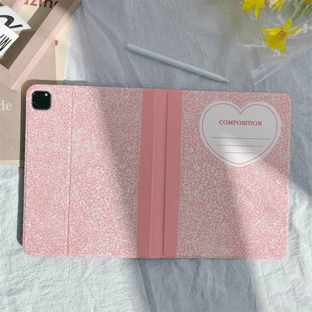 A pink composition notebook iPad case with a pencil holder is shown on a light gray fabric.