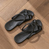 A pair of black foldable EVA travel slippers resting on a wooden floor.