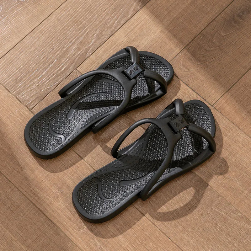 A pair of black foldable EVA travel slippers resting on a wooden floor.