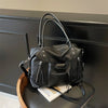 A black soft leather plaid crossbody bag with an adjustable strap resting on a dark surface.
