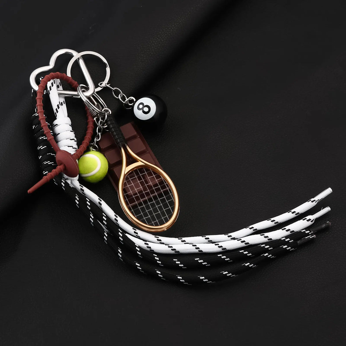 A metal 8-ball keychain featuring a black finish, attached to a leather cord and a tennis racket.