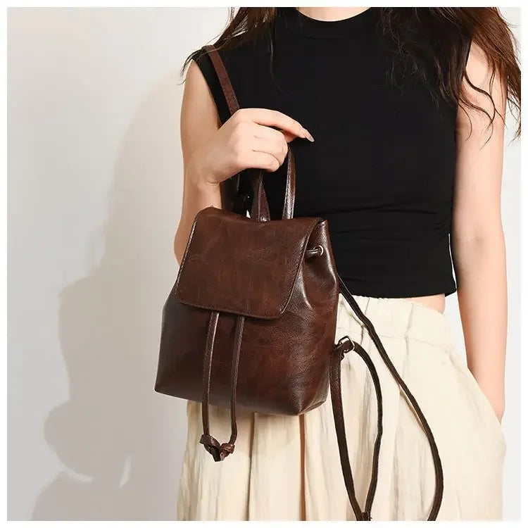 Une femme tient un petit sac à dos de type pochette marron artistique sur un fond clair.