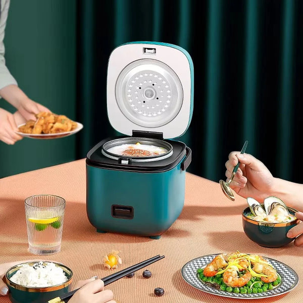 Una olla arrocera eléctrica compacta mostrada sobre una mesa con comida y utensilios.