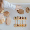 A hand places wooden spinning tops labeled with Hebrew letters onto a white surface.