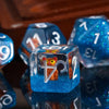 A close-up of a blue resin die featuring an orange animal figurine, surrounded by other colorful dice.