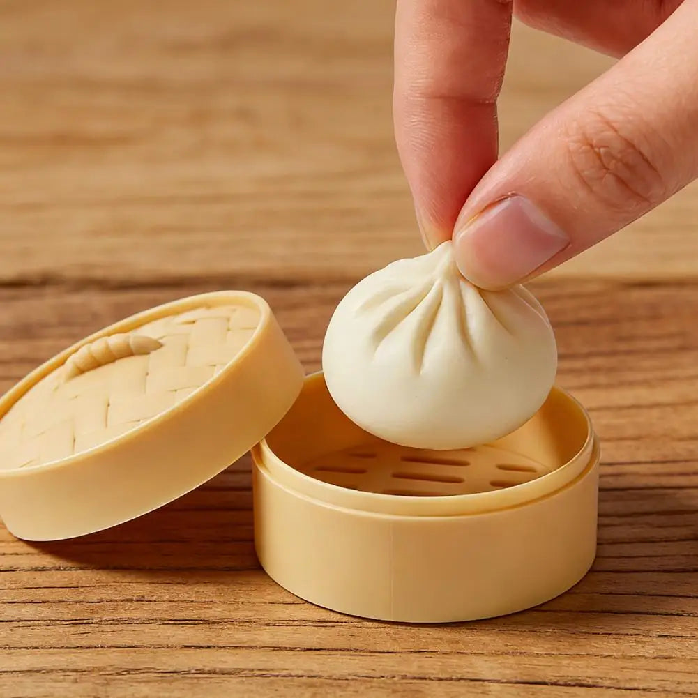 A hand is squeezing a white dumpling squishy toy, which is placed in its yellow mini steamer basket.