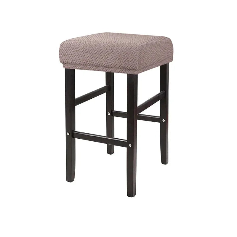 A square bar stool featuring a beige woven fabric slipcover with an elastic edge.