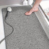 A gray textured bathroom floor mat with a chrome hose and a bare foot resting on it.