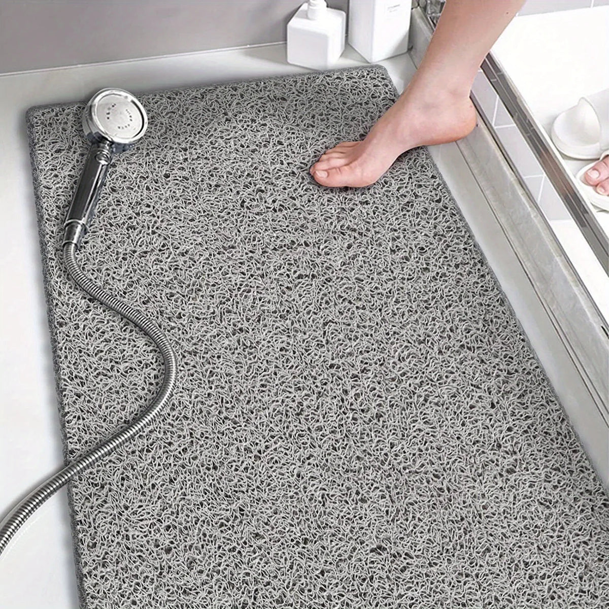 A gray textured bathroom floor mat with a chrome hose and a bare foot resting on it.