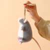 A hand is holding a gray and white plush mouse stuffed animal with a keychain loop.