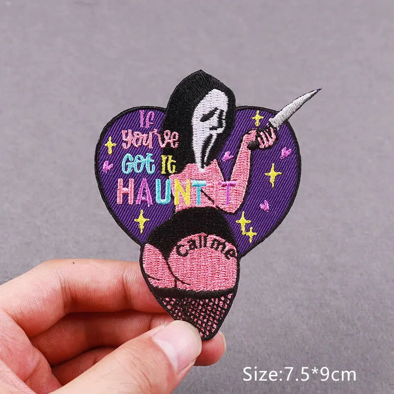 A hand holds an embroidered patch featuring a stylized skull with text on a purple background.
