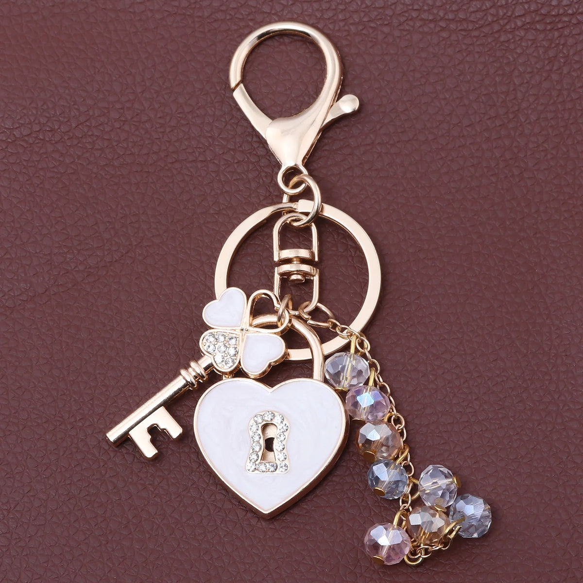 Gold-toned keychain featuring a key, a heart charm, and a flower design on a brown leather background.