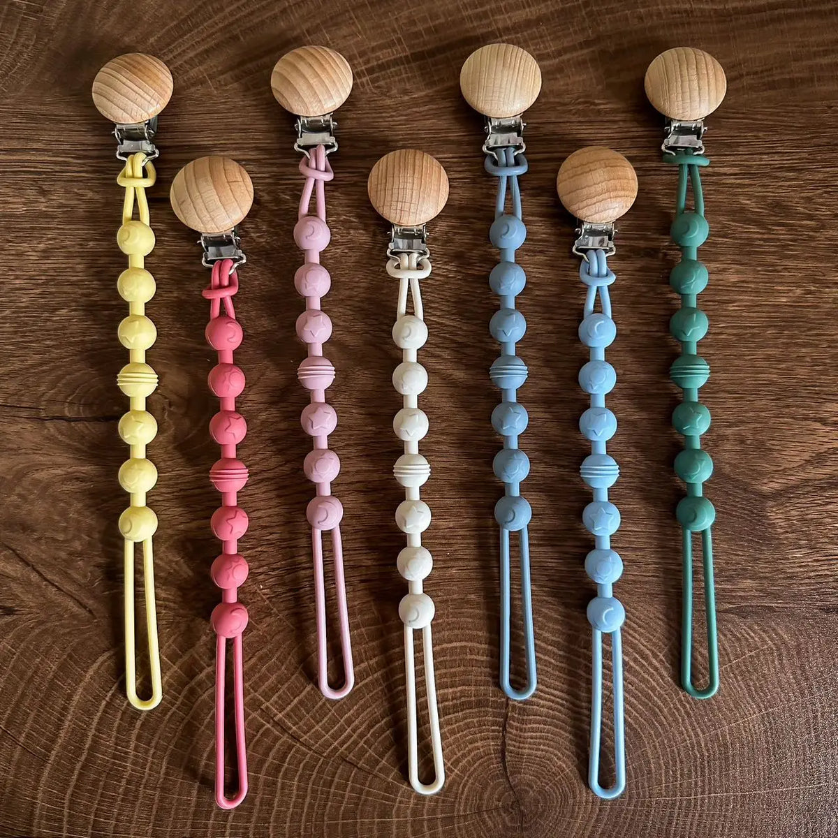 A collection of silicone pacifier clips with wooden teethers in various pastel colors arranged vertically.