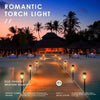 A wooden pathway lined with glowing torch lights leading toward a tropical silhouette at sunset.