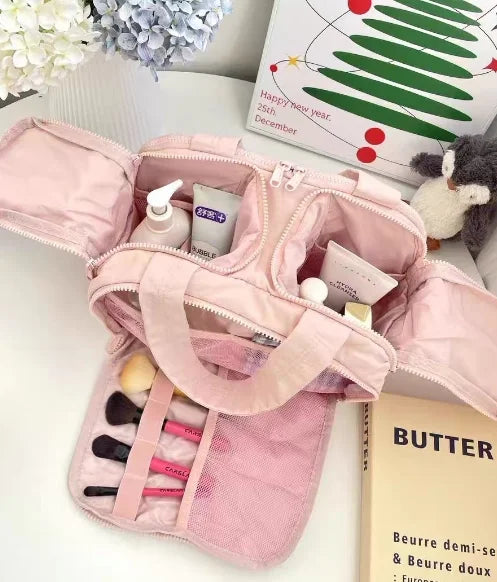 A pink travel makeup bag with a wide opening is shown open, revealing cosmetic products and a skincare item.