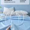 A hand is touching a light blue cooling quilt on a bed, illustrating the fabric's thinness and lightness.