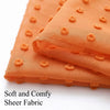 Orange sheer fabric with pom pom details shown in a folded textile.