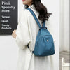 A woman wearing a white oversized shirt and black hat carries a teal mini backpack with a strap.
