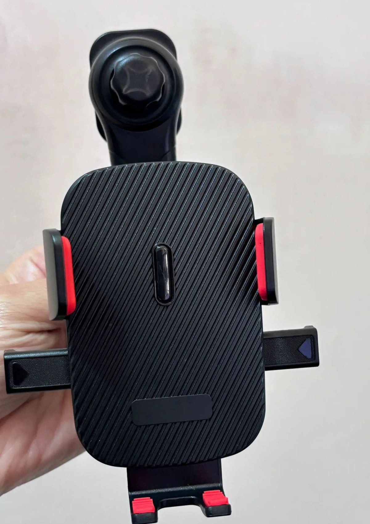 A black universal gravity car phone holder with a hook clip is held in a hand.