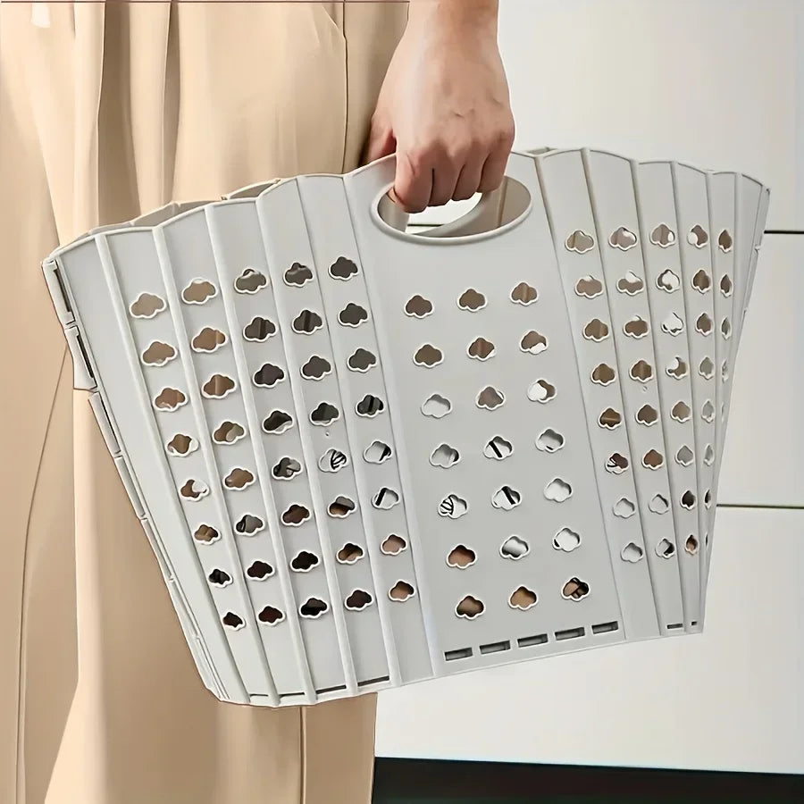A white folding laundry basket with handles is being held by a person, shown in a side view.