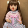 A lifelike 50 cm full silicone baby doll with long brown hair and a pink floral dress