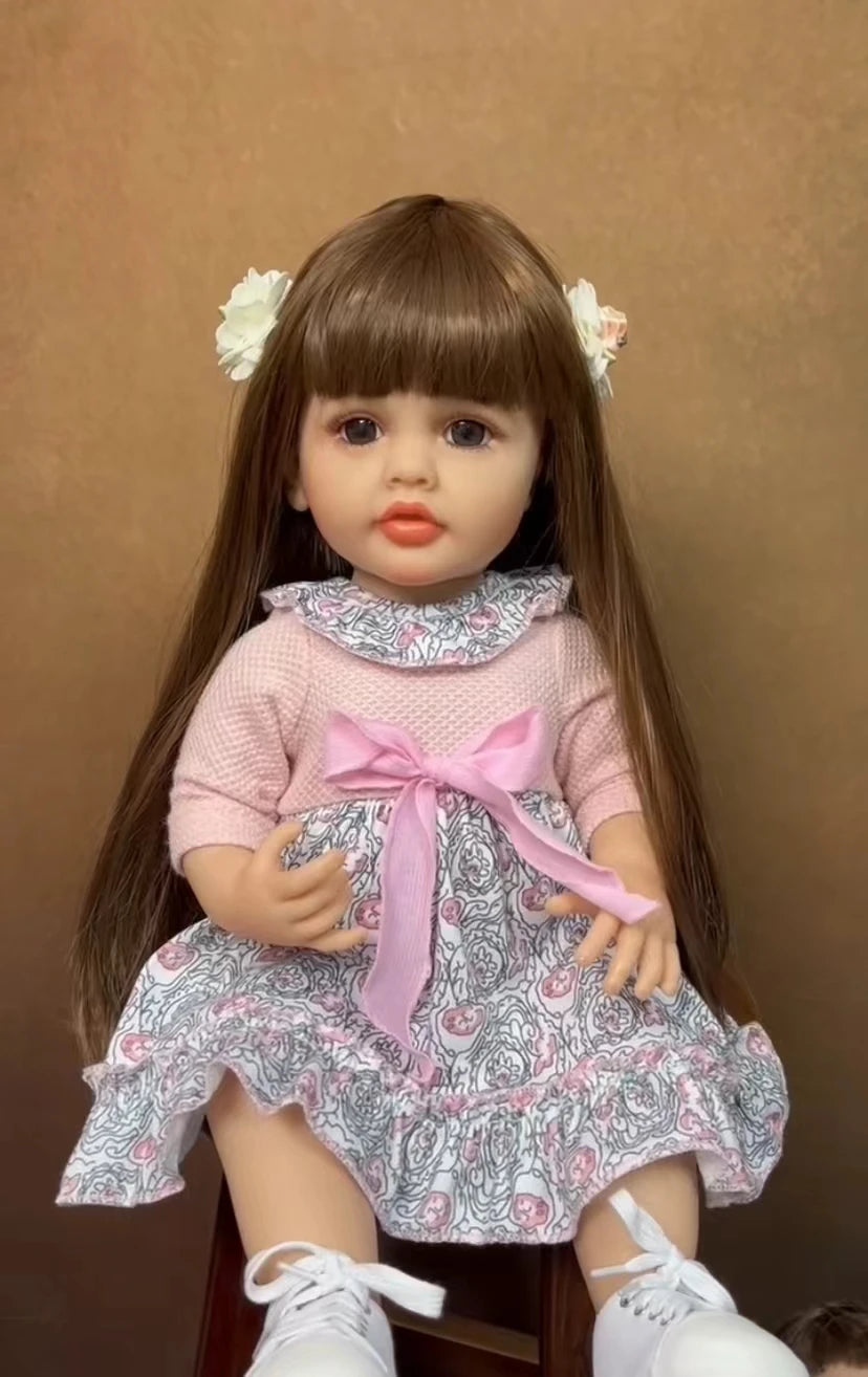 A lifelike 50 cm full silicone baby doll with long brown hair and a pink floral dress