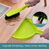 A hand is using a bright lime green compact handheld dustpan and brush set to clean a corner.