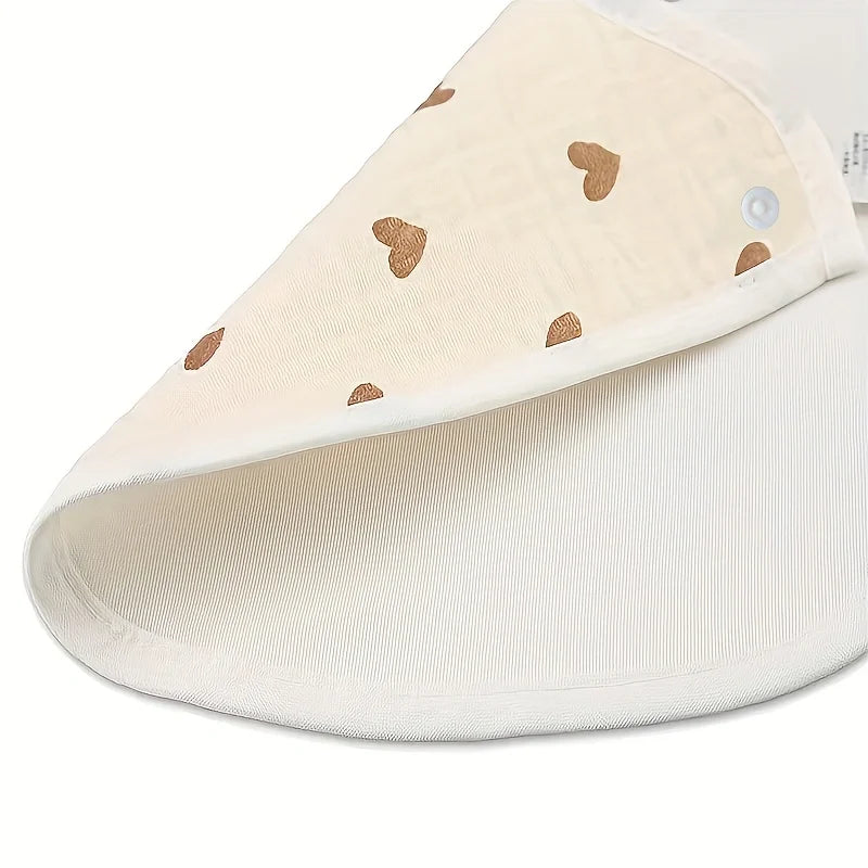 A close-up view of a cream-colored baby cotton gauze bib with small brown heart embroidery and a waterproof backing.
