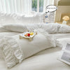 White ruffled duvet cover set with pillows and a small plate of fruit on a bed