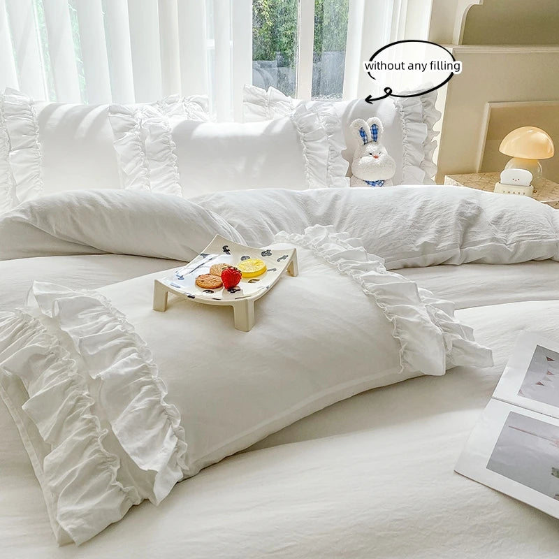 White ruffled duvet cover set with pillows and a small plate of fruit on a bed