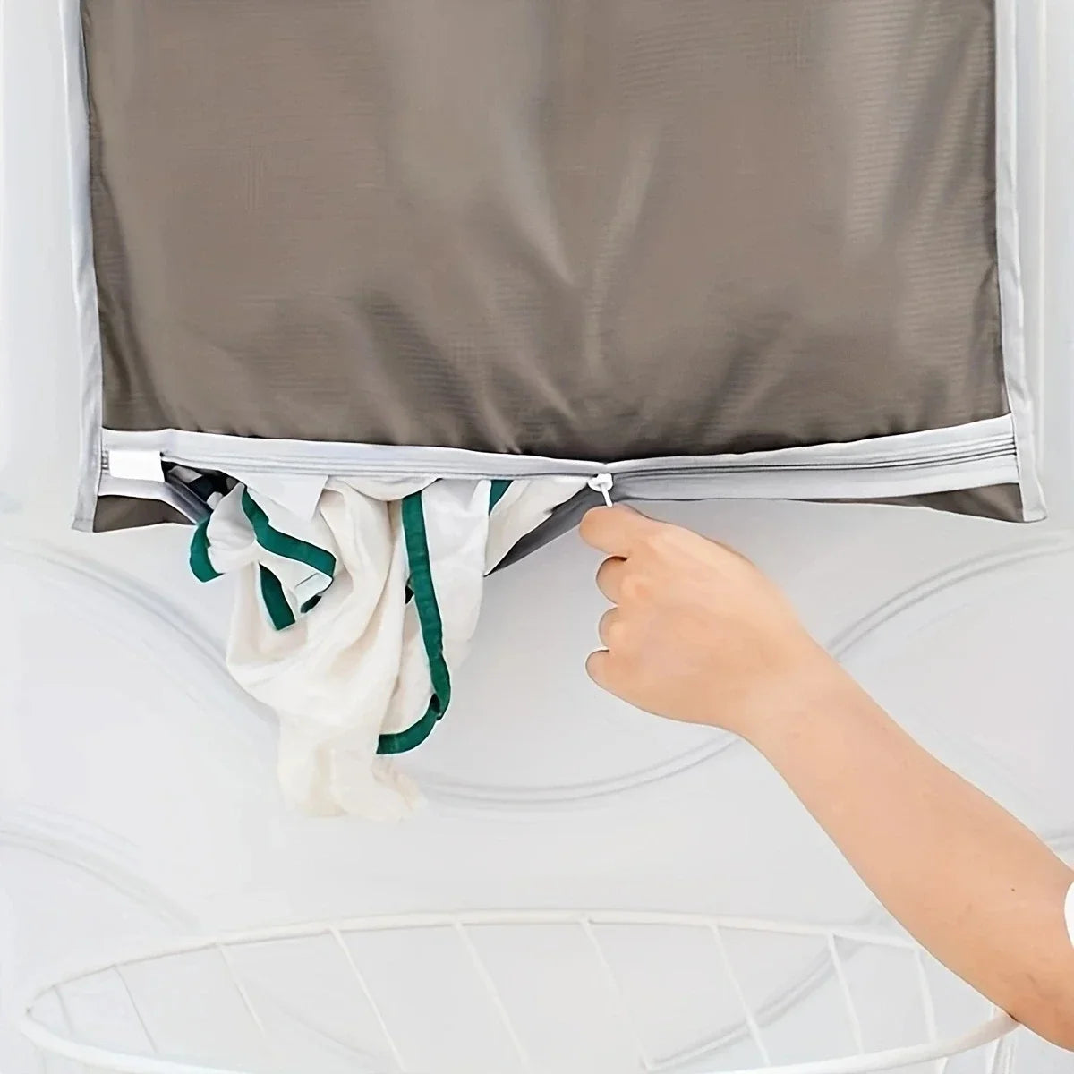 A hand opens a gray wall-mounted laundry storage bag to reveal white towels inside.