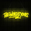 A neon sign spelling out THE WORLD IS YOURS in yellow light, hanging against a dark grid background.