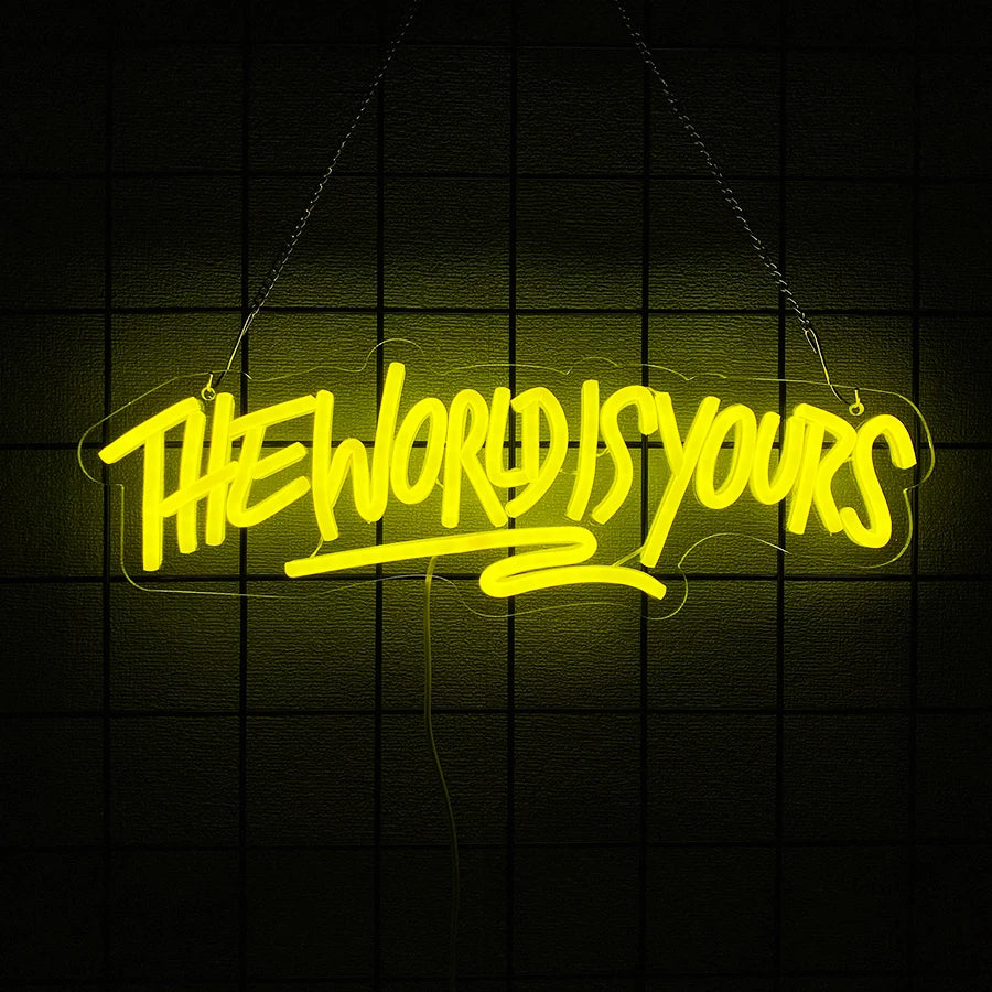 A neon sign spelling out THE WORLD IS YOURS in yellow light, hanging against a dark grid background.