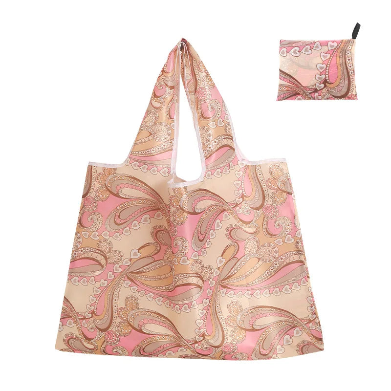 A beige reusable shopping tote bag featuring a pink and gold paisley pattern, with a matching small carry pouch.