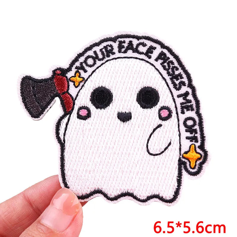 A white ghost embroidered patch with black outline and pink accents on a hand.