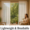 A woman sits on a wooden bench looking out through sheer white curtains at a lush green garden view.